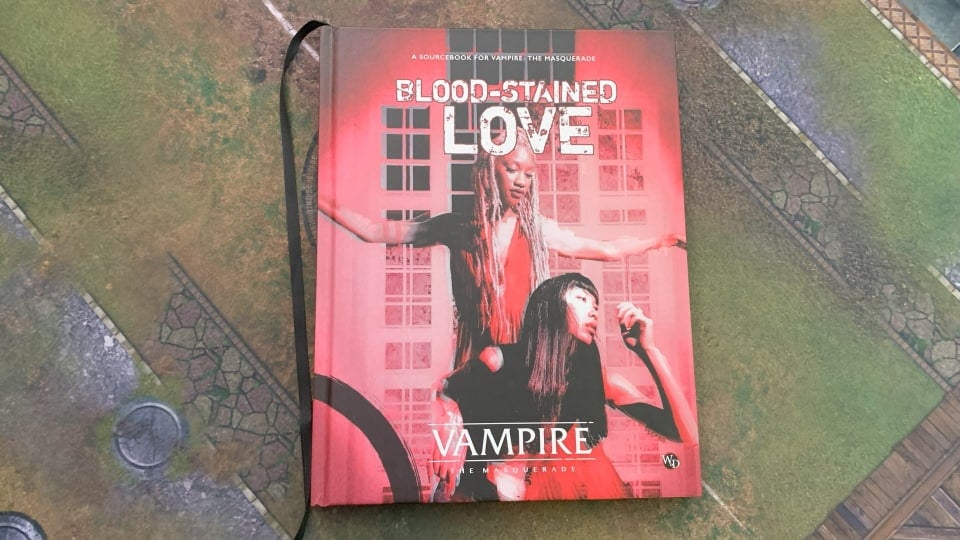 A hardcover copy of Vampire: The Masquerade Blood-Stained Love sitting on a gaming mat.